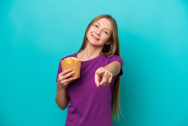 Jeune femme russe attraper des frites isolées sur fond bleu pointant vers l'avant avec une expression heureuse