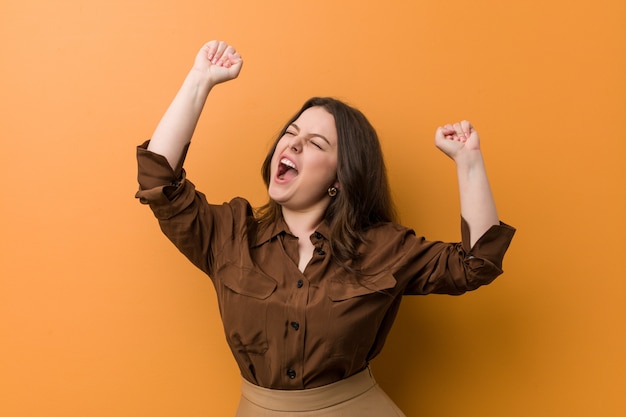 Jeune femme russe bien roulée célébrant une journée spéciale, saute et lève les bras avec énergie.