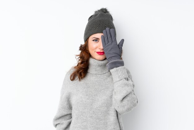 Jeune femme russe avec un chapeau d'hiver sur fond blanc isolé couvrant un œil à la main