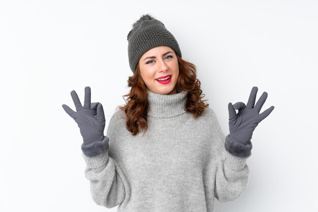 Jeune femme russe avec chapeau d'hiver sur isolé montrant un signe ok avec les doigts