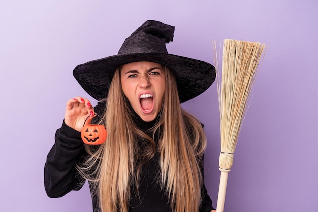 Photo jeune femme russe déguisée en sorcière tenant un balai et une citrouille isolée sur fond violet