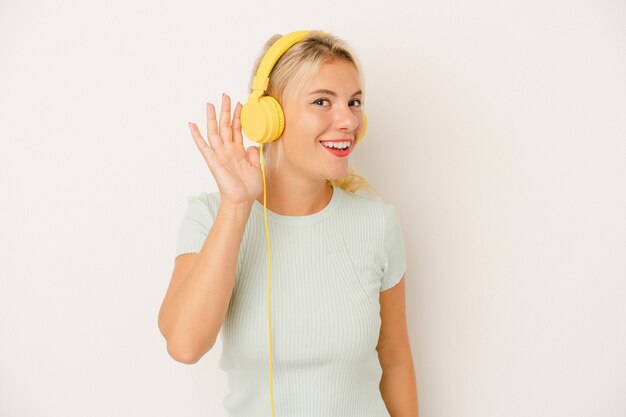 Jeune femme russe écoutant de la musique isolée sur fond blanc essayant d'écouter un potin.