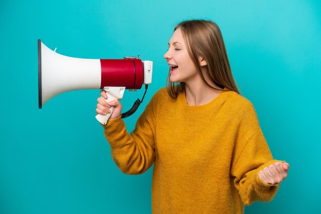 Jeune femme russe isolée sur fond bleu criant à travers un mégaphone pour annoncer quelque chose en position latérale