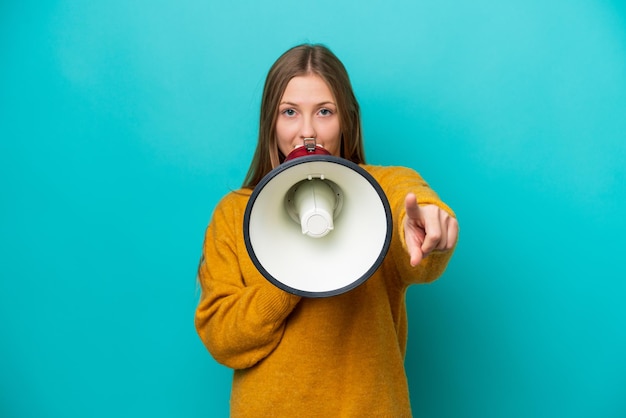 Jeune femme russe isolée sur fond bleu criant à travers un mégaphone pour annoncer quelque chose tout en pointant vers l'avant