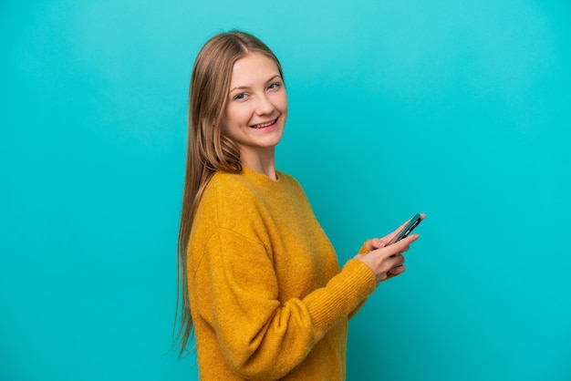 Jeune femme russe isolée sur fond bleu envoyant un message ou un e-mail avec le mobile