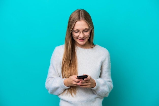 Jeune femme russe isolée sur fond bleu envoyant un message avec le mobile