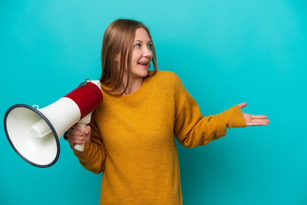 Jeune femme russe isolée sur fond bleu tenant un mégaphone et avec une expression faciale surprise