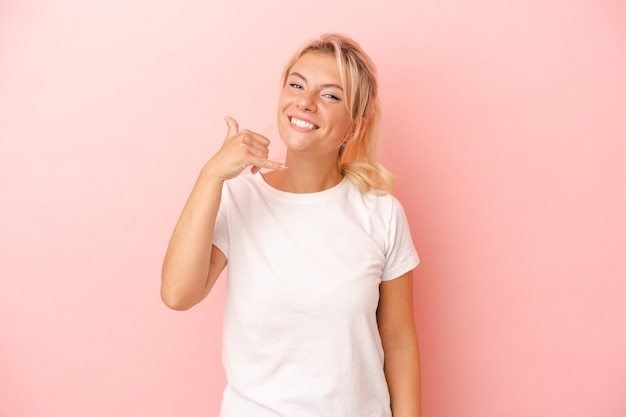 Jeune femme russe isolée sur fond rose montrant un geste d'appel de téléphone portable avec les doigts.