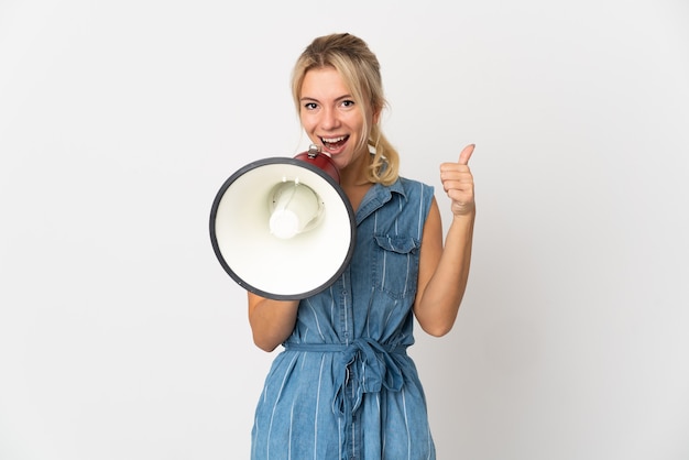 Jeune femme russe isolée sur un mur blanc criant à travers un mégaphone pour annoncer quelque chose et avec le pouce vers le haut