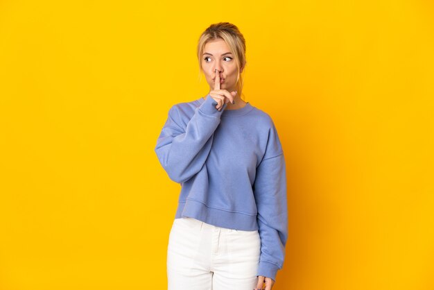 Jeune femme russe isolée sur un mur jaune montrant un signe de silence geste mettant le doigt dans la bouche