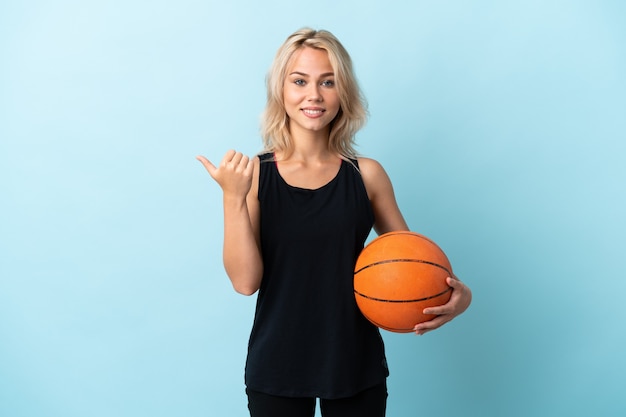 Jeune femme russe jouant au basket isolé sur fond bleu pointant vers le côté pour présenter un produit