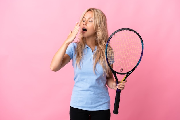 Jeune femme russe jouant au tennis isolé sur mur violet bâillement et couvrant la bouche grande ouverte avec la main