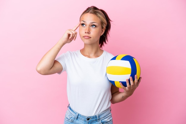 Jeune femme russe jouant au volleyball isolée sur fond rose ayant des doutes et pensant