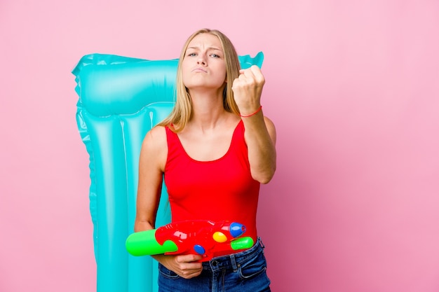 Jeune femme russe jouant avec un pistolet à eau avec un matelas pneumatique montrant le poing à la caméra, une expression faciale agressive.