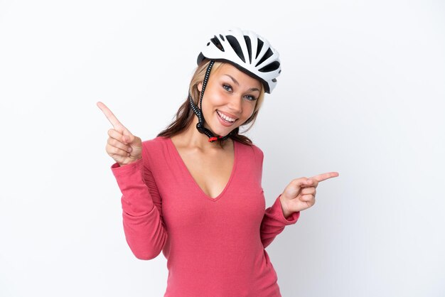 Jeune femme russe portant un casque de vélo isolé sur fond blanc pointant le doigt vers les latéraux et heureux