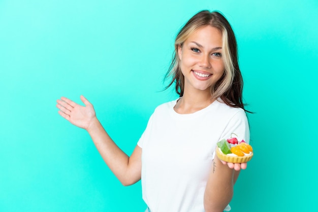 Jeune femme russe tenant un bonbon aux fruits isolé sur fond bleu tendant les mains sur le côté pour inviter à venir