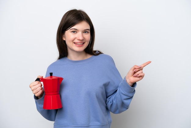 Jeune femme russe tenant une cafetière isolée sur fond blanc, pointant le doigt sur le côté