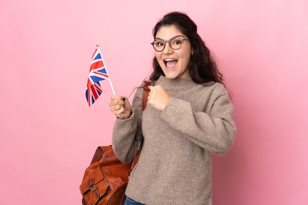 Jeune femme russe tenant un drapeau du Royaume-Uni isolé sur fond rose célébrant une victoire