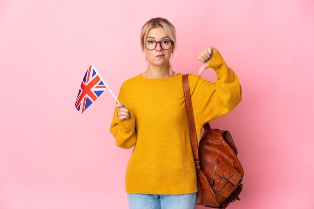 Jeune femme russe tenant un drapeau du Royaume-Uni isolé sur fond rose montrant le pouce vers le bas avec une expression négative