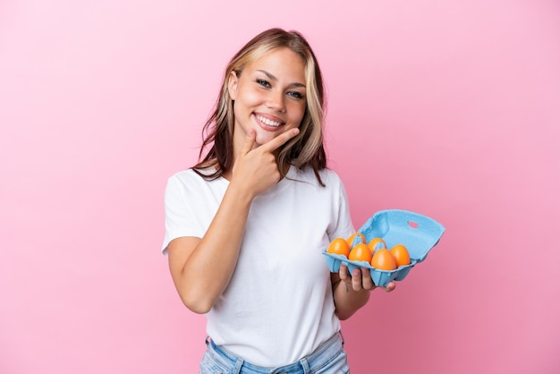 Jeune femme russe tenant des oeufs isolés sur fond rose heureux et souriant