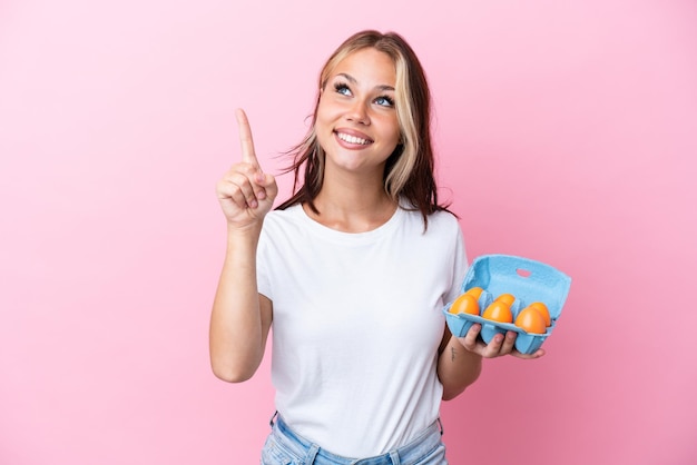 Jeune femme russe tenant des oeufs isolés sur fond rose pointant vers le haut une excellente idée