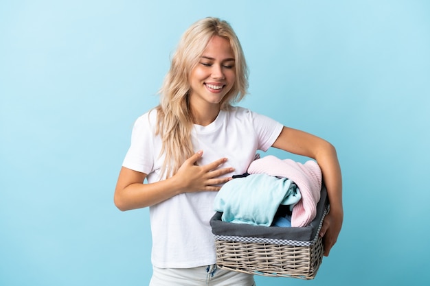 Jeune femme russe tenant un panier de vêtements isolé sur bleu souriant beaucoup