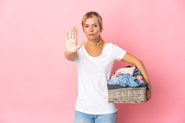 Jeune femme russe tenant un panier de vêtements isolé sur mur rose faisant le geste d'arrêt