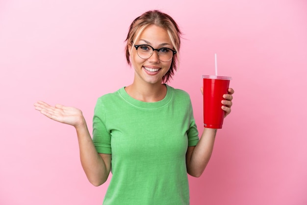 Jeune femme russe tenant un rafraîchissement isolé sur fond rose avec une expression faciale choquée