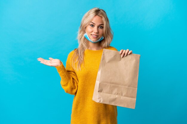 Jeune femme russe tenant un sac d'épicerie isolé sur bleu holding copyspace imaginaire sur la paume pour insérer une annonce