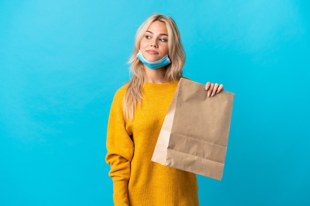 Jeune femme russe tenant un sac d'épicerie isolé sur bleu. Portrait