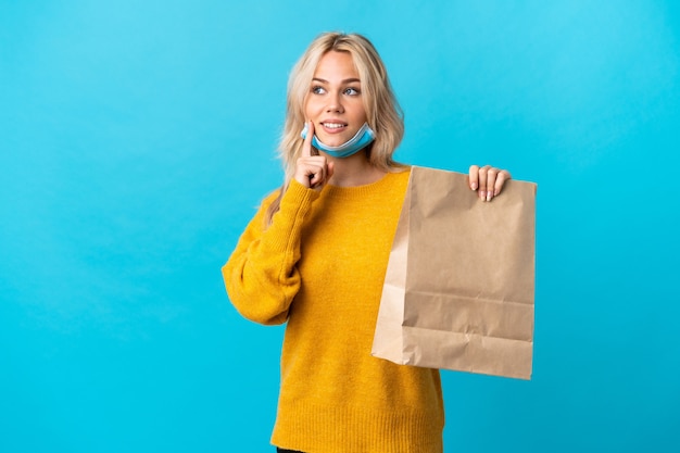 Jeune femme russe tenant un sac d'épicerie isolé sur fond bleu en pensant à une idée tout en regardant