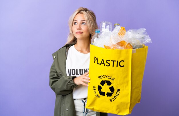 Jeune femme russe tenant un sac de recyclage plein de papier à recycler isolé sur mur violet et en levant