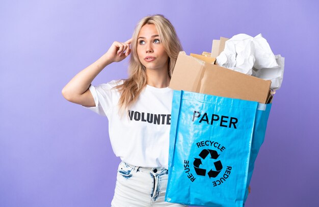 Jeune femme russe tenant un sac de recyclage plein de papier à recycler isolé sur violet ayant des doutes et de la réflexion