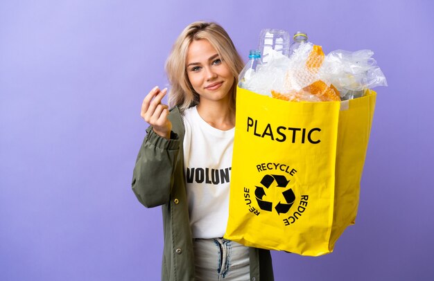 Jeune femme russe tenant un sac de recyclage plein de papier à recycler isolé sur violet faisant de l'argent geste