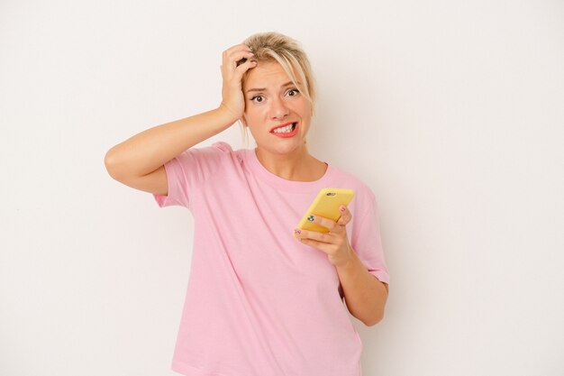 Jeune femme russe tenant un téléphone portable isolé sur fond blanc étant choquée, elle s'est souvenue d'une réunion importante.