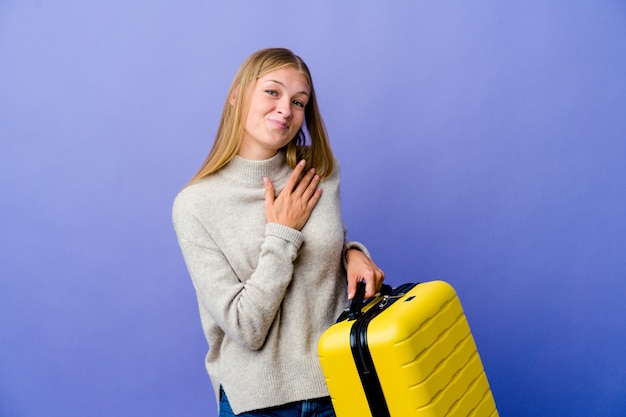 Jeune femme russe tenant une valise pour voyager a une expression amicale, en appuyant sur la paume de la main contre la poitrine. Concept d'amour.