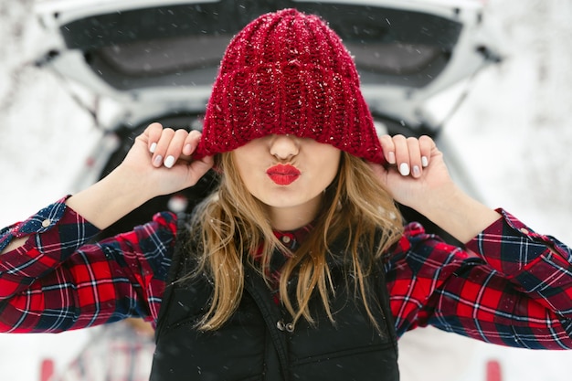 La jeune femme s'amuse dans la forêt d'hiver tire un chapeau rouge sur ses yeux et rit