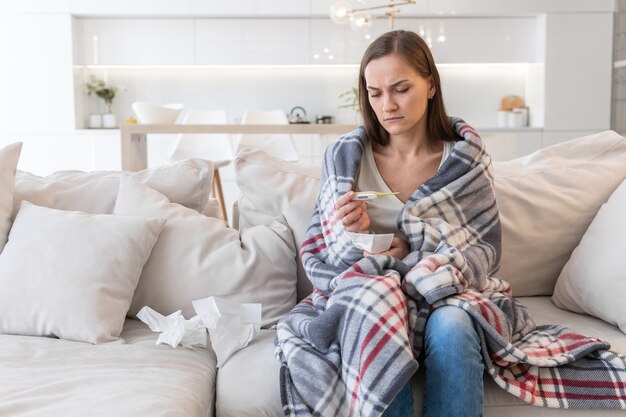 La jeune femme s'assied sur le sofa et regarde le thermomètre