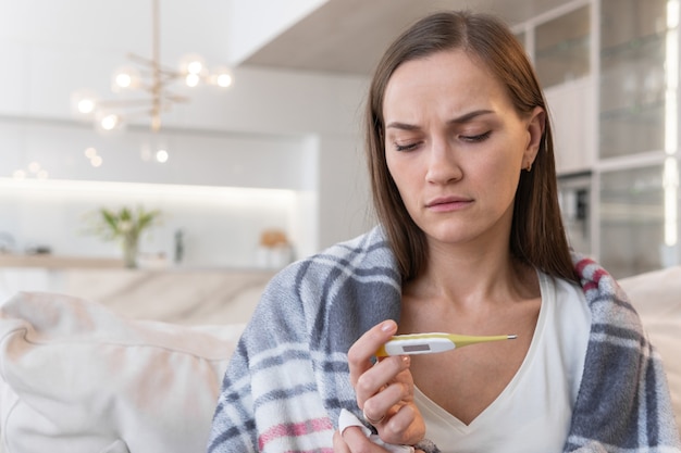 La jeune femme s'assied sur le sofa et regarde le thermomètre