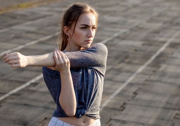 Jeune femme s'entraînant sur le stade en été. Sportive, étirements, échauffement avant l'exercice à l'extérieur. Mode de vie sain