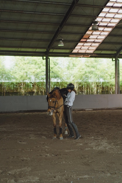 Une jeune femme s'entraîne à l'équitation dans l'arène. Jeune femme caucasienne en vêtements formels faisant de l'équitation à travers l'arène sablonneuse. Un cheval de race pour le sport équestre. La sportive à cheval