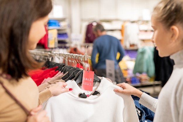 Jeune femme et sa fille à la recherche de sweat-shirt blanc sur cintre avec cinquante pour cent de réduction tout en choisissant de nouveaux vêtements décontractés