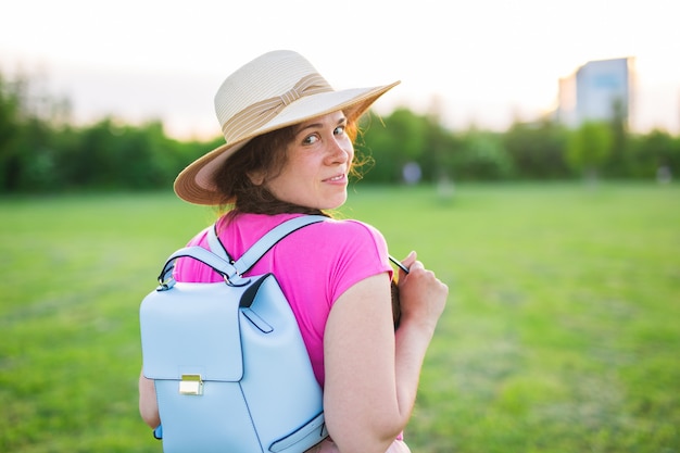 Jeune femme avec sac à dos bleu et chapeau profitant de la vue arrière de la campagne