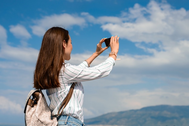 Jeune femme avec sac à dos prend la photo d'un paysage