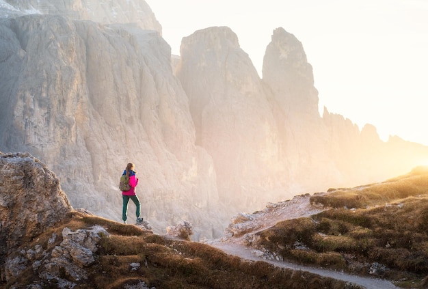 Jeune femme avec sac à dos sur le sentier de montagne et canyon de montagne au coucher du soleil Automne dans les Dolomites Italie Paysage coloré avec une fille sur le chemin des rochers du soleil doré à l'automne Trekking et randonnée