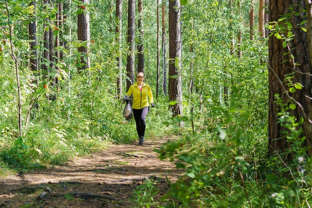 Jeune femme avec un sac poubelle à la main faisant du jogging le long d'un sentier forestier tout en se pavanant dans un parc