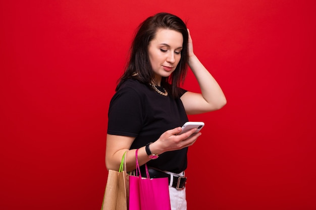 Une jeune femme avec un sac à provisions et un téléphone à la main sur fond rouge