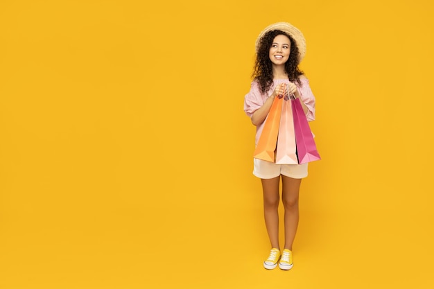 Jeune femme avec des sacs de boutique sur fond jaune