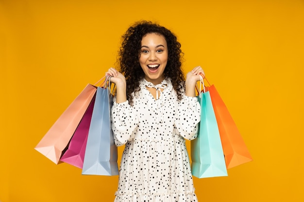 Jeune femme avec des sacs de boutique sur fond jaune