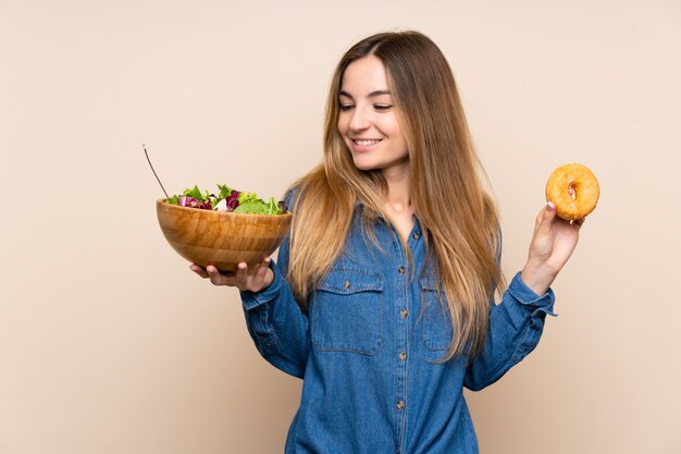 Jeune femme avec une salade sur un mur isolé et tenant un beignet